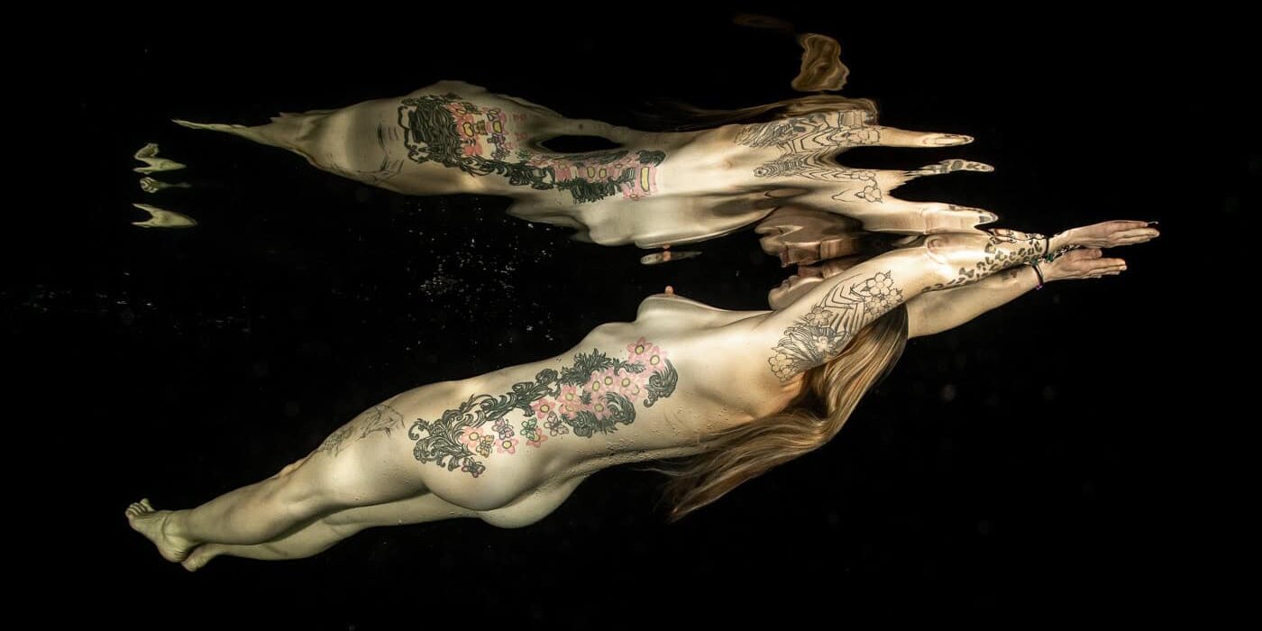 Naakte vrouw-tattoos-onderwater Naakte vrouw onder water met tattoos en zwarte achtergrond