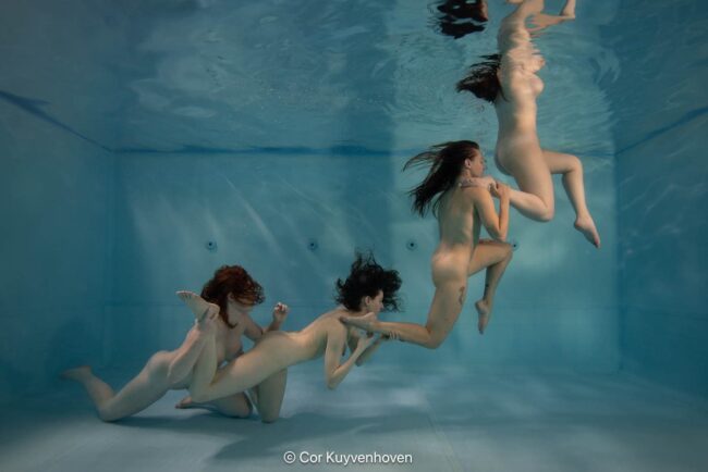Verlichte nude kunst onderwaterfotografie van meerdere vrouwen die een menselijke keten vormen. Nude vrouwen onder water, creatief kunstwerk, menselijke keten, onderwaterfotografie, expressief, artistiek en esthetisch, diversiteit en kwetsbaarheid.