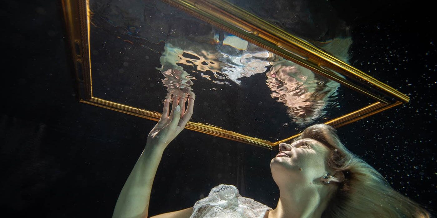 Een vrouw onderwater met spiegel en gouden lijst, symboliseert creativiteit en kunstzinnigheid, vastgelegd door Cor Kuyvenhoven voor inspirerende kunst- en lifestylebeelden.