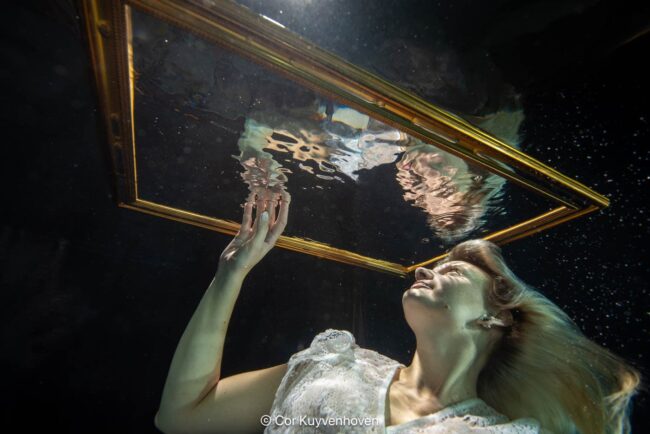 Creatieve onderwaterfotografie voor marketingcampagnes Een vrouw onderwater met spiegel en gouden lijst, symboliseert creativiteit en kunstzinnigheid, vastgelegd door Cor Kuyvenhoven voor inspirerende kunst- en lifestylebeelden.