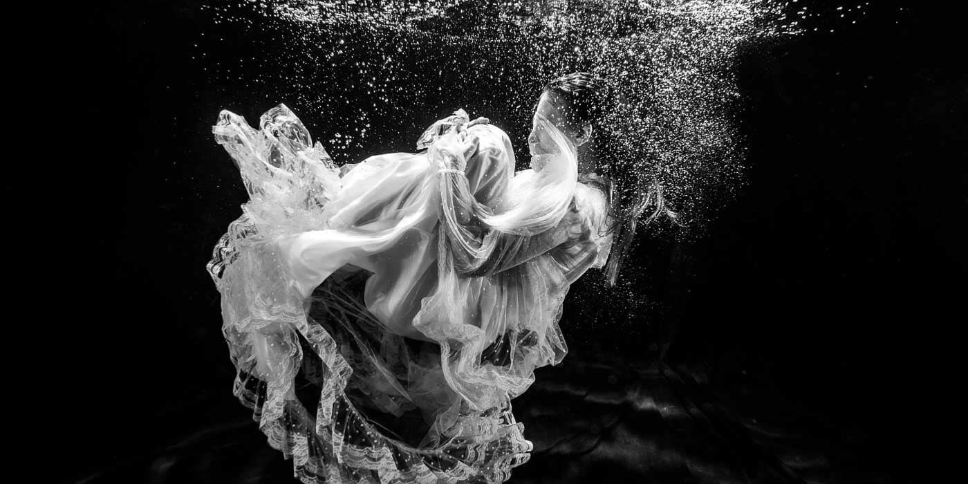 Elegante vrouw in jurk onderwater. Kunstvolle foto van een vrouw in een jurk onder water met zwevende stof en bubbels, creatief en artistiek, geschikt voor fotografie, mode en kunstliefhebbers.