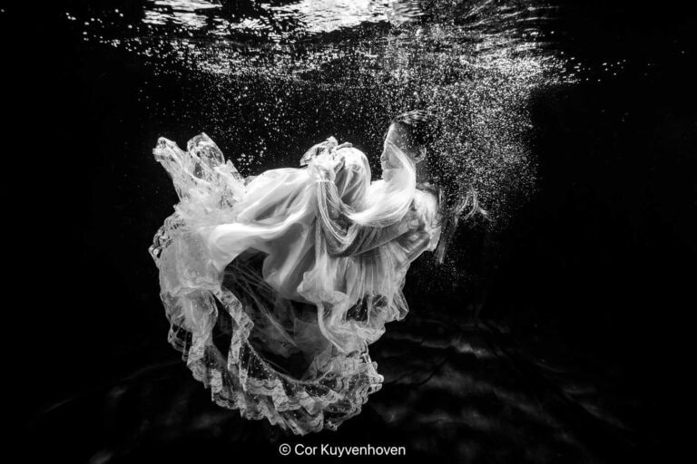Elegante vrouw in jurk onderwater. Kunstvolle foto van een vrouw in een jurk onder water met zwevende stof en bubbels, creatief en artistiek, geschikt voor fotografie, mode en kunstliefhebbers.