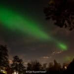 Noorderlicht, aurora borealis, boven bomen en huis in Nederland, nachtelijke hemel met groene lichtstralen en sterren.