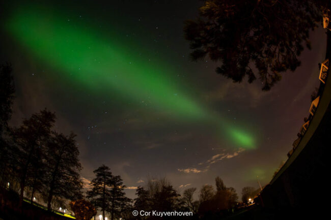 Noorderlicht, aurora borealis, boven bomen en huis in Nederland, nachtelijke hemel met groene lichtstralen en sterren.