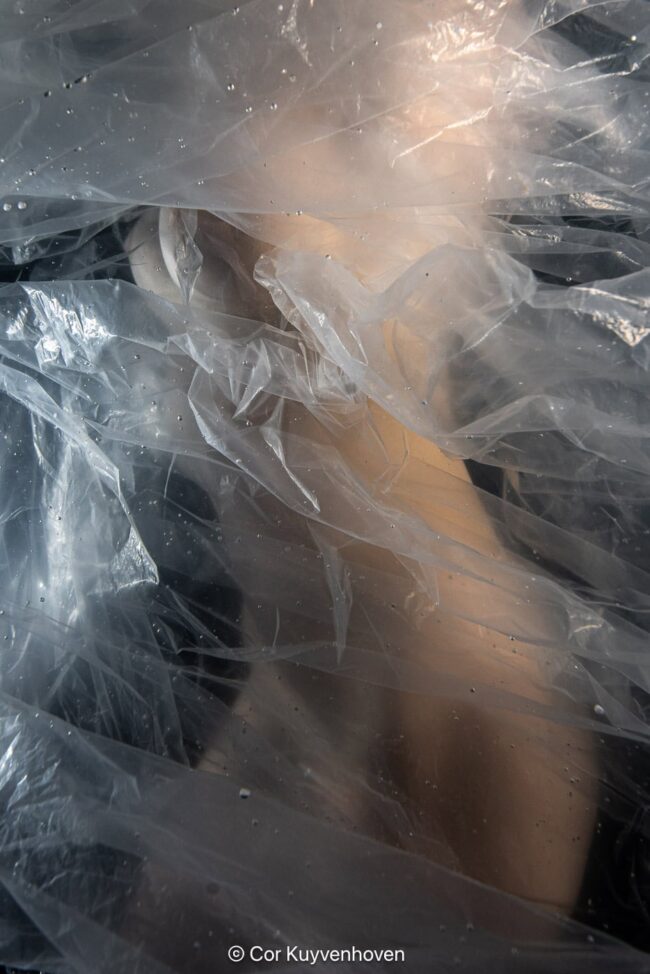 Onderwater kunstfoto van een menselijk lichaam omwikkeld met transparant plastic, zwevend in donker water, surrealistische fotografie door Cor Kuyvenhoven.