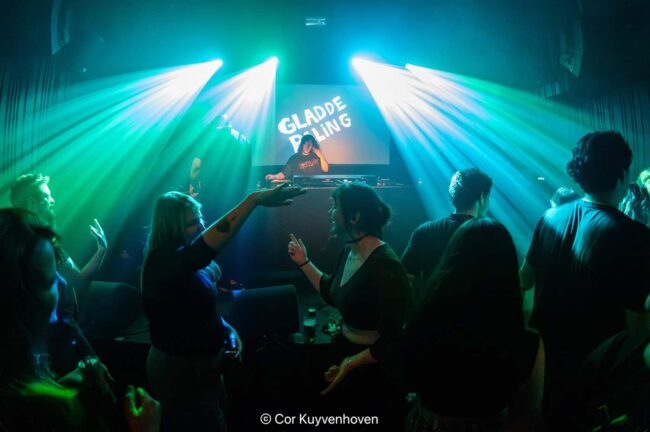 Gladde paling met feestvierders onder kleurrijke lichten en DJ achter de draaitafel.