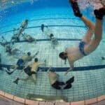 Onderwaterhockey in een zwembad tijdens een onderwaterhockeywedstrijd, met meerdere spelers die bal en water verkennen, onder water en in beweging.