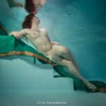 Een vrouw drijft ontspannen in een zwembad, omgeven door turquoise water, met een groene en gouden jurk die haar elegantie benadrukt.