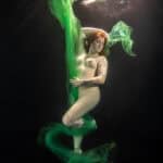 Onderwaterportret van een vrouw met groene stof die zweeft in het water, artistiek en creatief vastgelegd voor visuele impact.