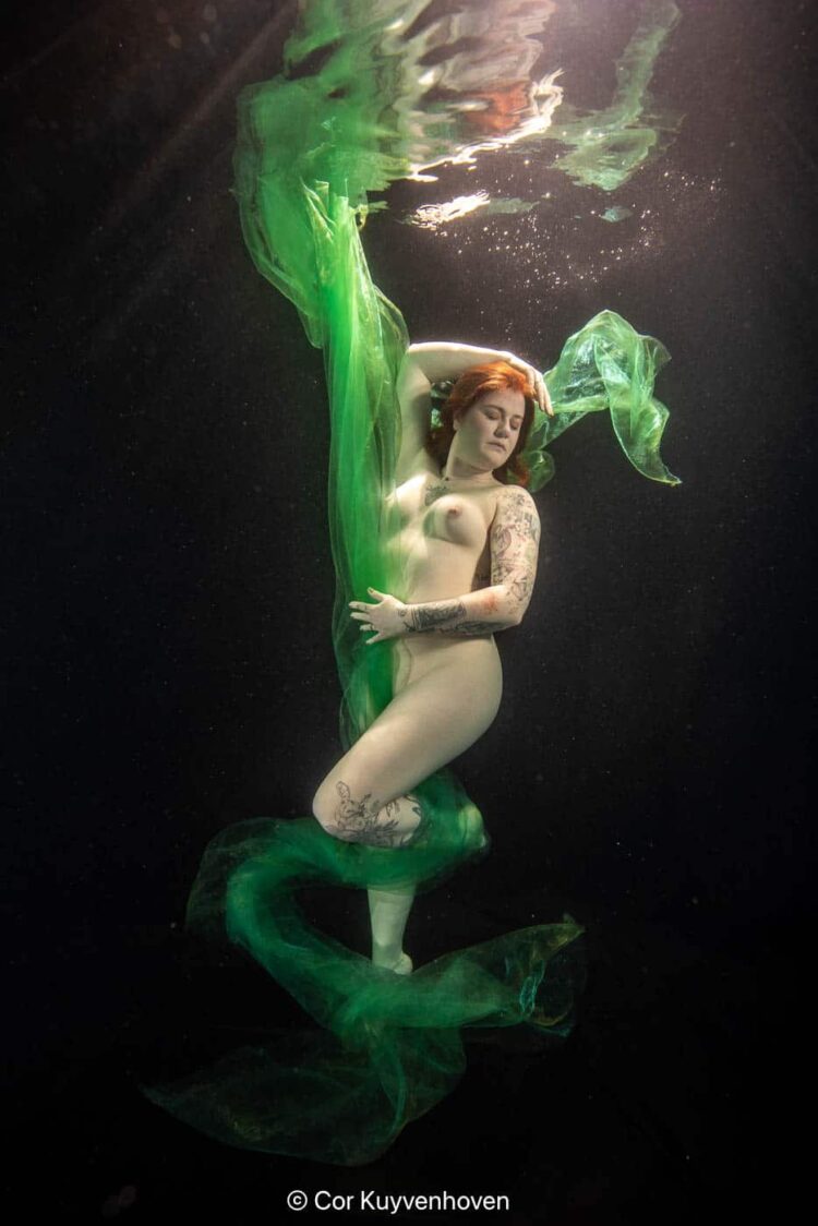 Onderwaterportret van een vrouw met groene stof die zweeft in het water, artistiek en creatief vastgelegd voor visuele impact.