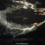 Zwemmer onder water, bewegend door het water met een gestrekte arm, in een donkere omgeving, professionele sportfotografie.